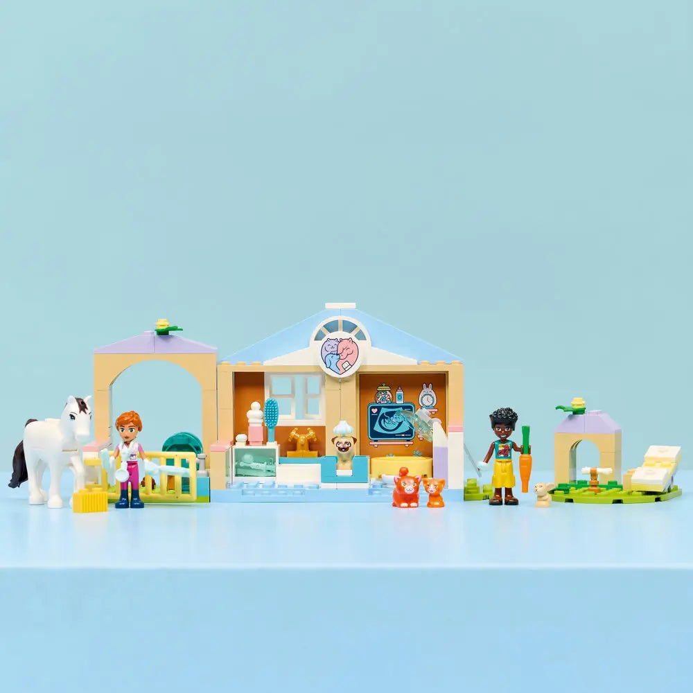 LEGO Friends Animal Vet Clinic fully assembled in tan and light blue plastic, compact clinic with archway, exam table, animal yard, and accessories, neatly arranged on a table against a soft blue background.