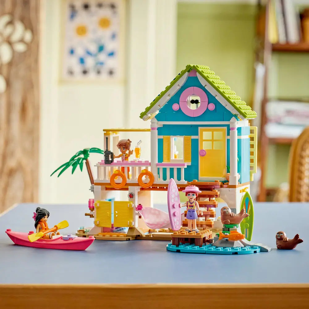 LEGO Friends Beach House with Seals fully assembled, bright turquoise, yellow, and green plastic house on stilts with balcony, dock, hammock, kayak, and seal animals, neatly displayed on a table in a cozy home interior.
