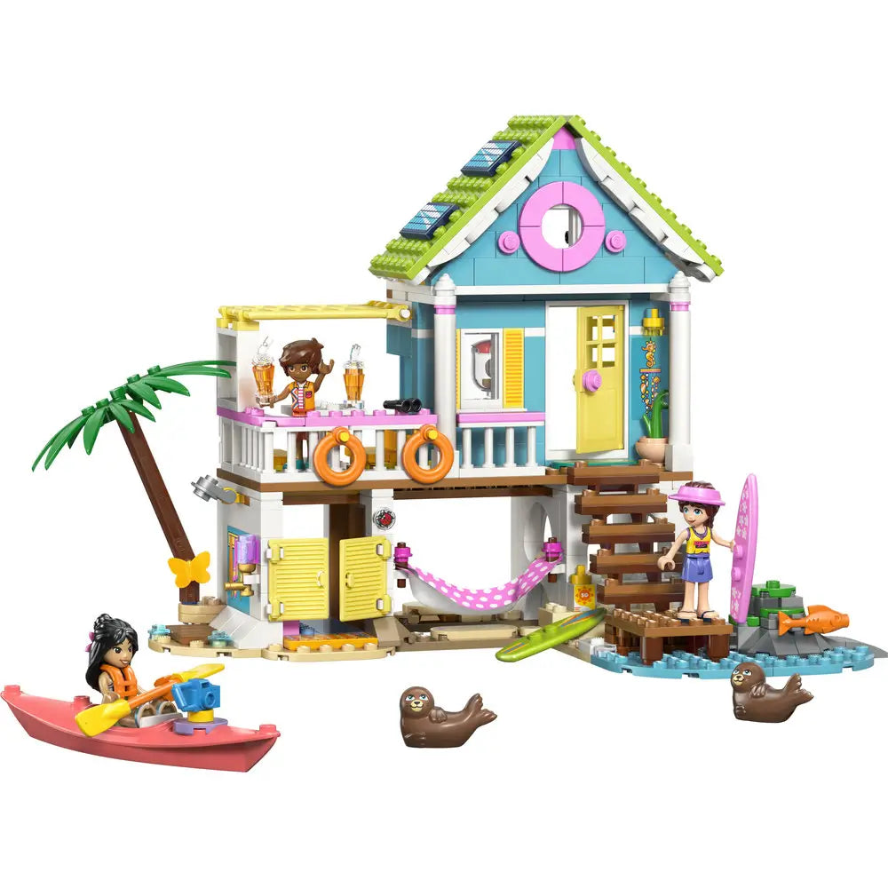 LEGO Friends beach house toy built in turquoise, yellow, and white plastic bricks, two-story stilted house with green roof, balcony, surfboards, kayak, and seal figures, designed for seaside play on a clean white background.