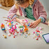LEGO Friends Candy & Cupcake Ferris Wheel 42700 in pink plastic is assembled by a child at a table, with ride parts, candy stalls, mini-dolls, accessories, and a tablet nearby.