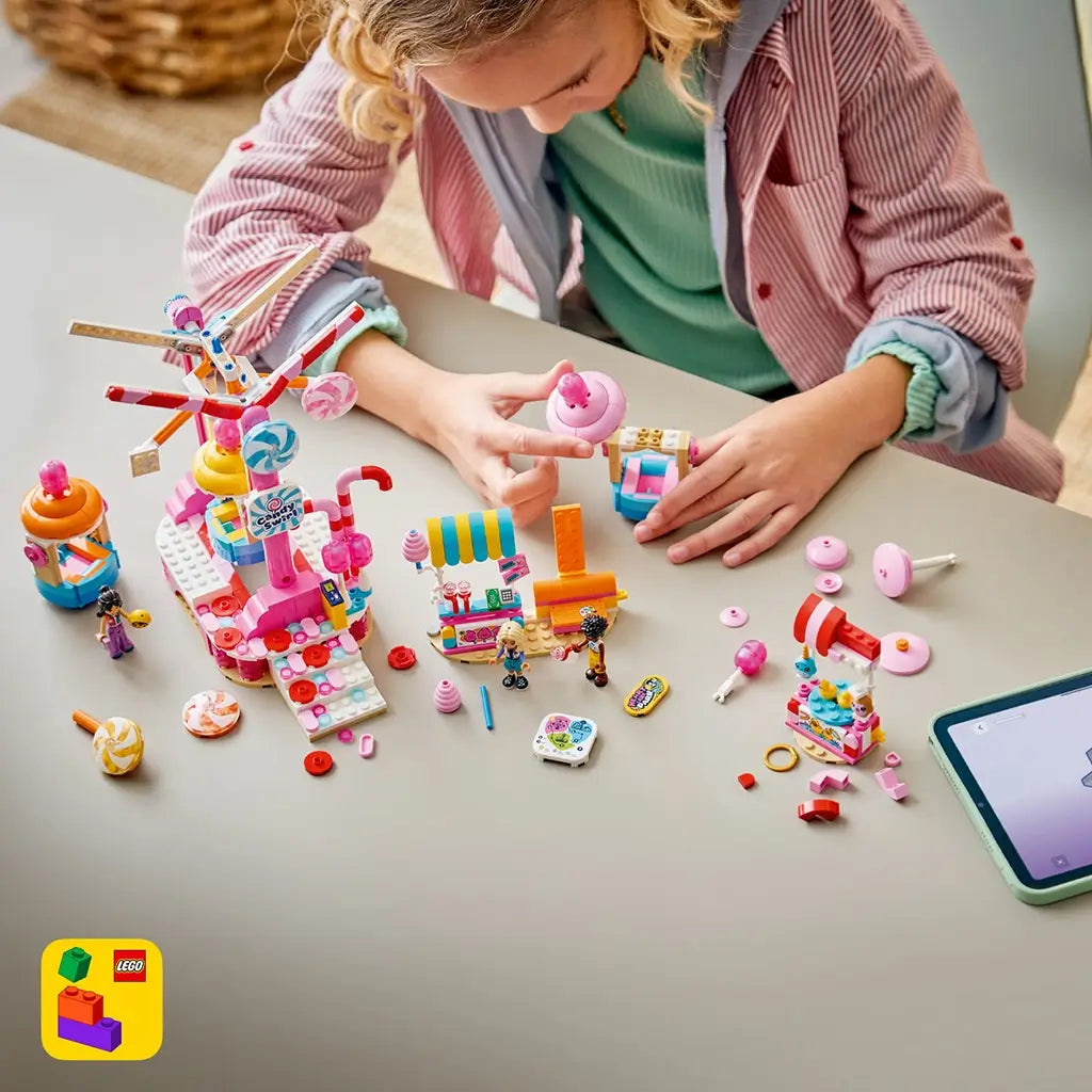 LEGO Friends Candy & Cupcake Ferris Wheel 42700 building set in pink and blue is assembled by a child, with loose ride parts, candy stalls, mini-dolls, and tablet on a table.