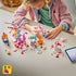 LEGO Friends Candy & Cupcake Ferris Wheel 42700 building set in pink and blue is assembled by a child, with loose ride parts, candy stalls, mini-dolls, and tablet on a table.