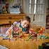 LEGO Friends Cozy Fall Forest Cabin building scene shows a child assembling the open brown and tan lodge at a table with figures, autumn trees, bicycle and scattered pieces.