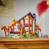 LEGO Friends Cozy Fall Forest Cabin display features a tall brown and tan lodge with purple roof, gray chimney, orange autumn trees, rocky stream, figures and bicycle on a wood surface.