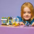 LEGO Friends Creative Flower Shop in green, pink and white plastic, with flower displays and tandem bicycle as a child plays with the set at a purple table.