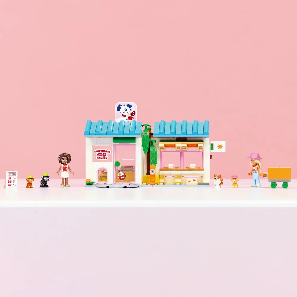 LEGO Friends dog treats bakery display showing a finished pastel bakery with blue tiled roofs, pink accents, service window, treat counter, menu sign, pet figures, minidolls, and a clean studio background.