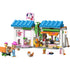 LEGO Friends Dog Treats Bakery playset showing pastel white, blue, pink, and tan plastic bricks forming a small dog bakery with tiled roofs, display counter, treat oven, menu sign, pet figures, and minidolls in a friendly shop setting.
