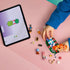 LEGO Friends Forest Tea Party set in green, orange and pastel plastic, partly assembled with loose pieces beside digital building instructions on a tablet.