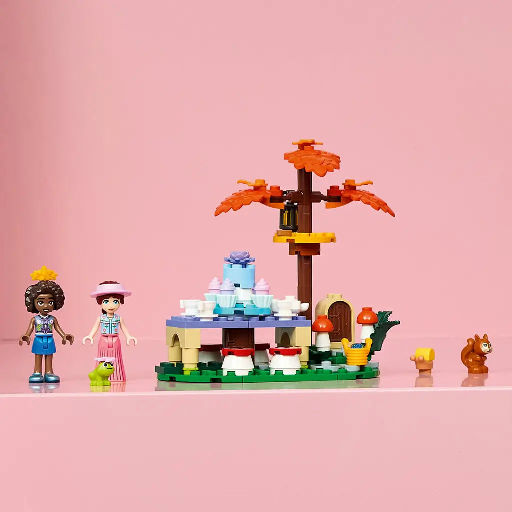 LEGO Friends Forest Tea Party set in green, brown and pastel plastic, with two mini-dolls, squirrel, frog, tea table and autumn tree displayed on a pink background.