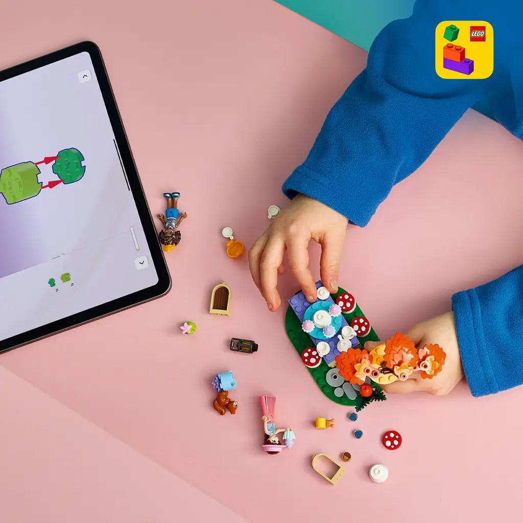 LEGO Friends Forest Tea Party set in green, orange and pastel plastic, under construction with loose figures and pieces beside digital instructions on a tablet.