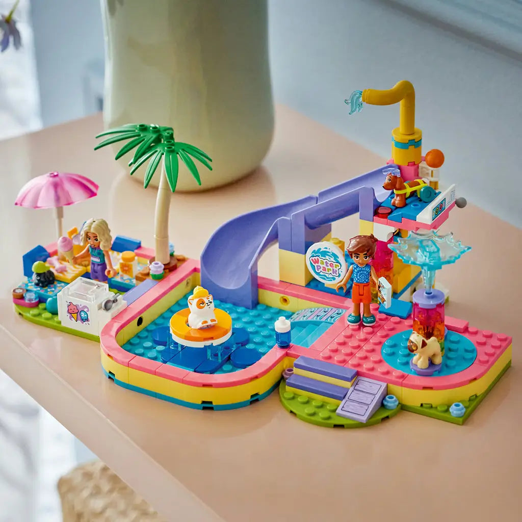 LEGO Friends Fun Water Park Day 42676 in pink, aqua and purple plastic, with pool, slide, splash features, palm tree, two mini-dolls and pet figures on a table.