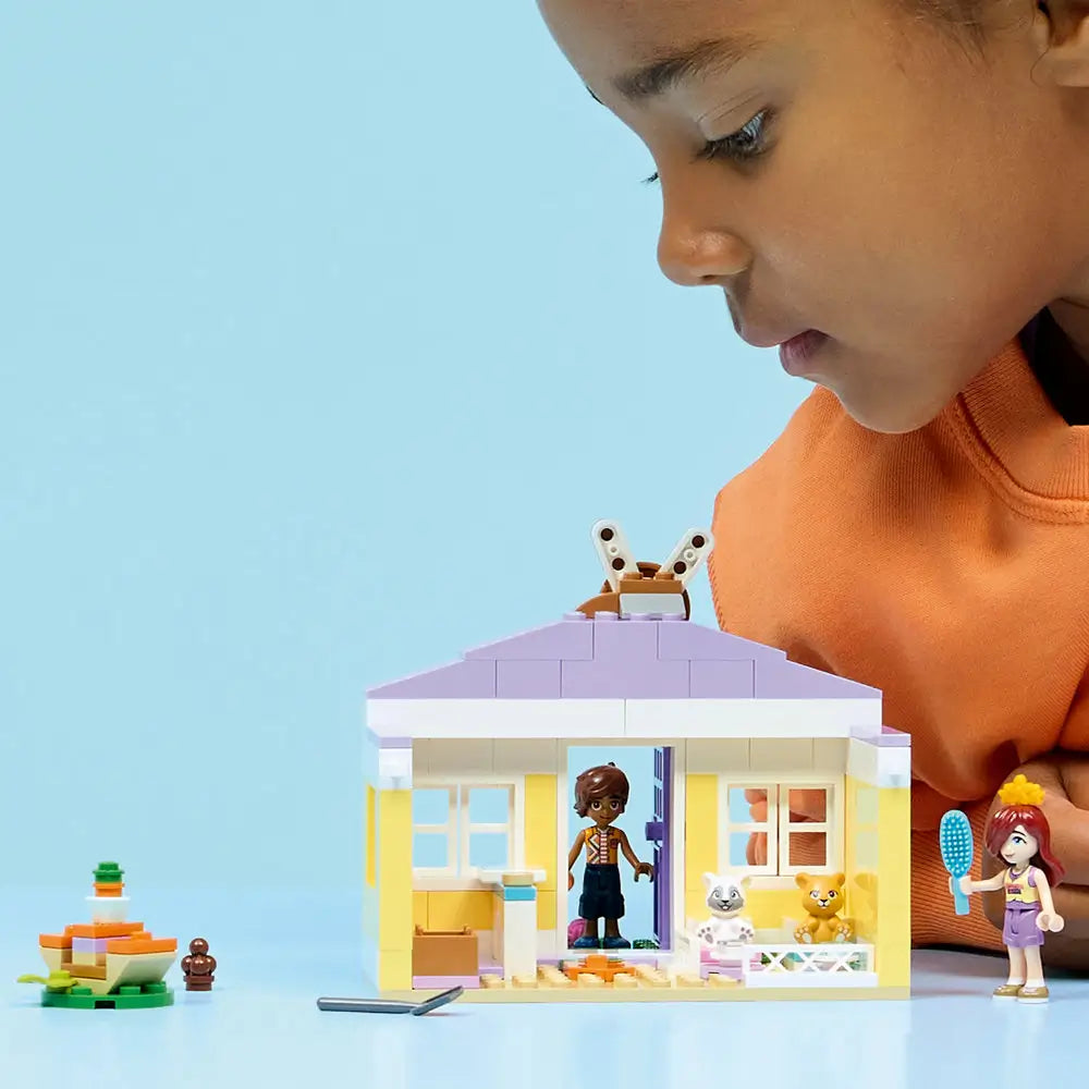 LEGO Friends playset lifestyle scene with a child playing with a completed bunny hotel, placing minifigures and animal figures inside rooms and garden spaces to act out pet care stories.