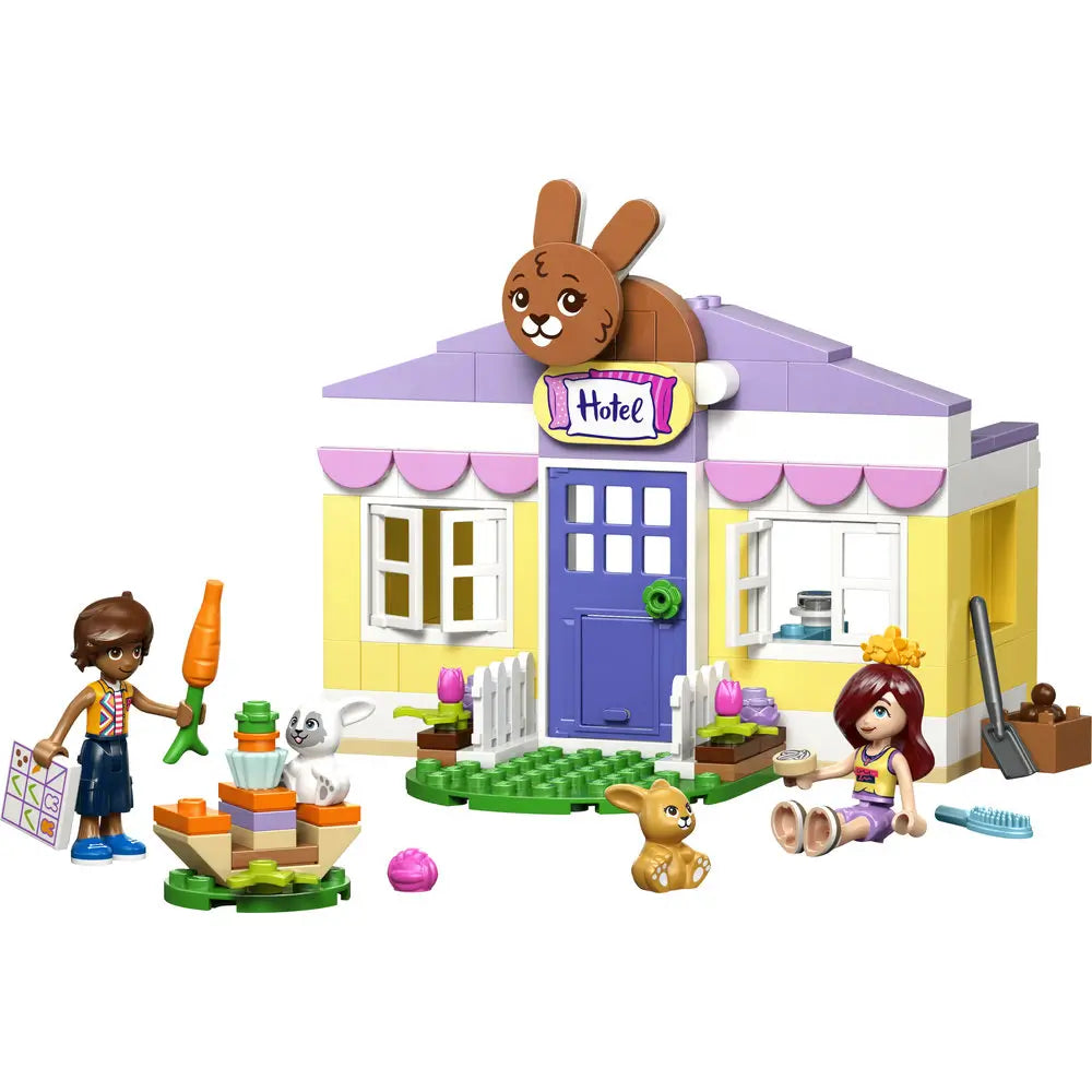 LEGO Friends Heartlake City Bunny Hotel playset showing pastel yellow, lavender, and white plastic bricks forming a small animal hotel with bunny sign, garden area, feeding station, accessories, and minifigures.