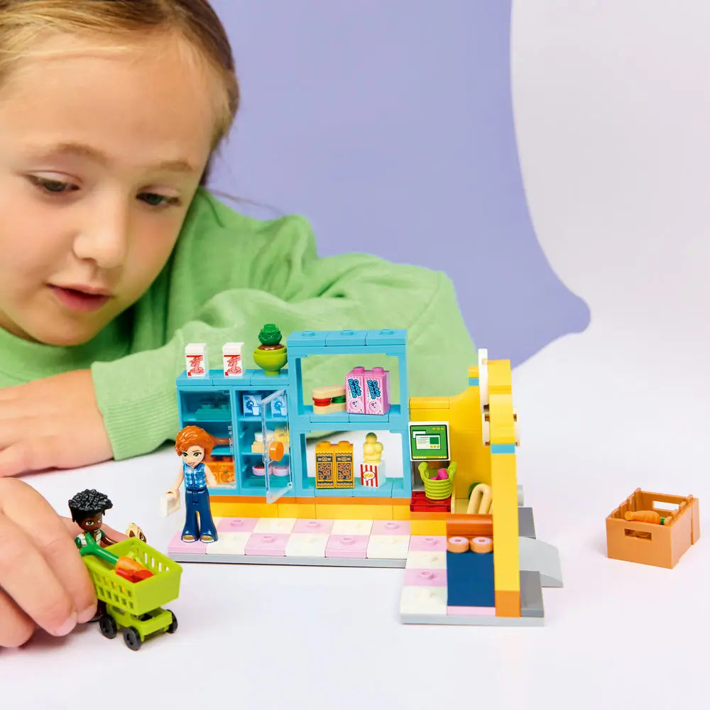 LEGO Friends playset lifestyle scene with a child interacting with a completed convenience store, moving minifigures, shopping cart, and accessories to act out grocery shopping and recycling stories.