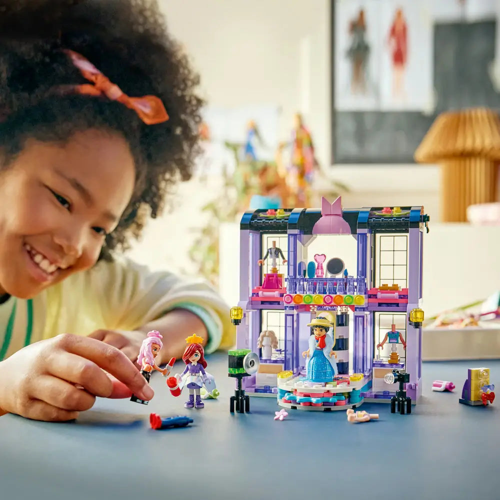 LEGO Friends playset lifestyle scene with a smiling child playing with a completed fashion show runway, posing minifigures on the rotating stage, using cameras, accessories, and costumes to act out fashion stories.
