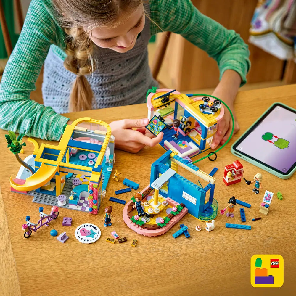 LEGO Friends Heartlake City Friends Club House playset shows colorful plastic rooms separated on a table, with blue, pink, and yellow bricks, mini dolls interacting, tech accessories, and a creative indoor play environment.
