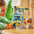 LEGO Friends Heartlake City Friends Club House lifestyle image shows a child building and playing with the blue and pink plastic club house, arranging mini dolls, slide, café items, and tech accessories on a tabletop.