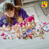 LEGO Friends Heartlake City Grand Hotel building scene shows a child assembling the pink, white and lavender hotel at a table with figures, loose bricks, wedding arch and luggage cart.