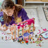LEGO Friends Heartlake City Grand Hotel playset in pink, white and lavender bricks is assembled on a table as a child builds beside figures, accessories, wedding arch and loose pieces.