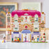 LEGO Friends Heartlake City Grand Hotel display features a pink, white and lavender three-story hotel with arched entrance, balconies, elevator, figures, luggage cart and wedding scene.