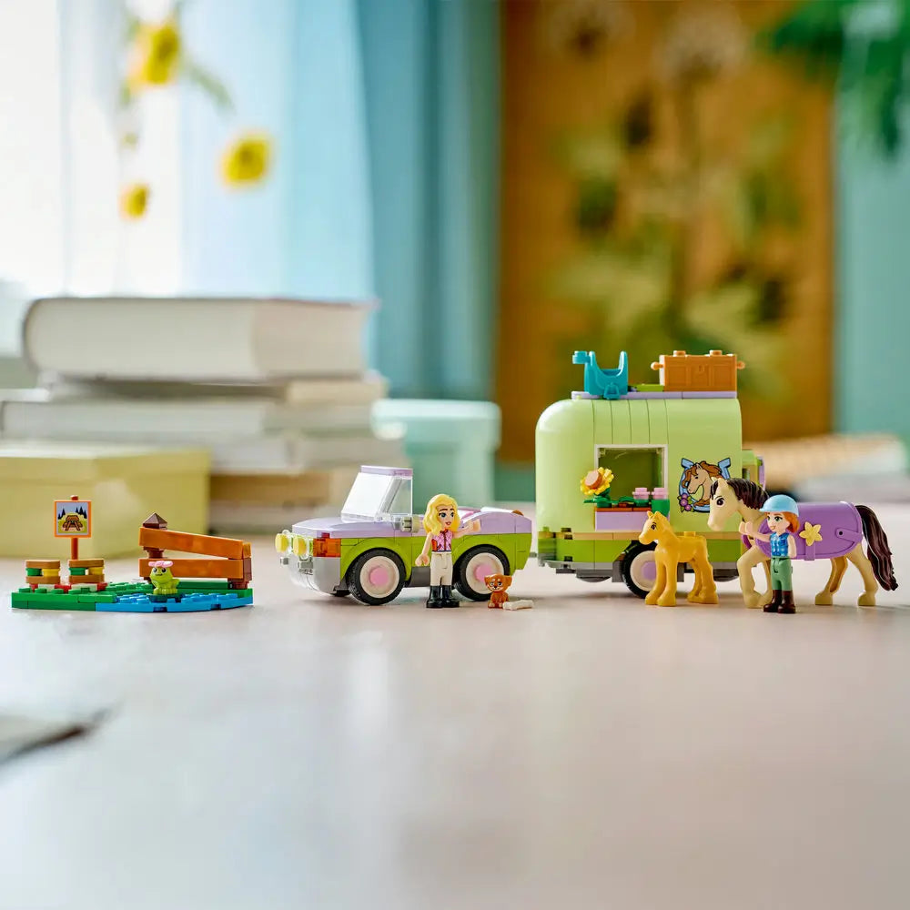 LEGO Friends Horse & Baby Foal Trailer fully assembled in light green and lavender plastic, compact car and trailer with opening roof, horse care accessories, and animal figures, neatly displayed on a table in a cozy home environment.