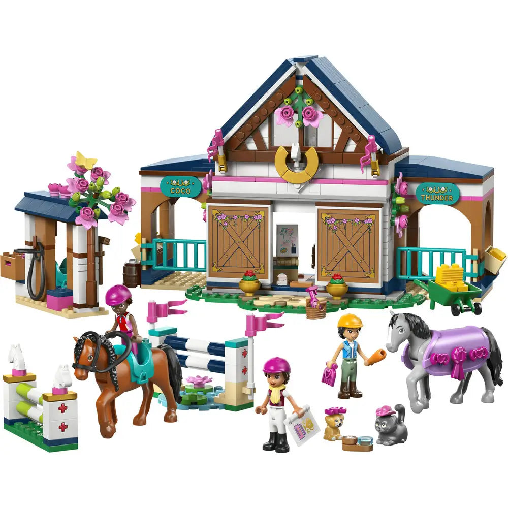 LEGO Friends Horse Stable and Riding Academy playset features tan, white, and blue plastic bricks forming a barn with stalls, arches, flower details, horses, riders, and outdoor equestrian training setting.