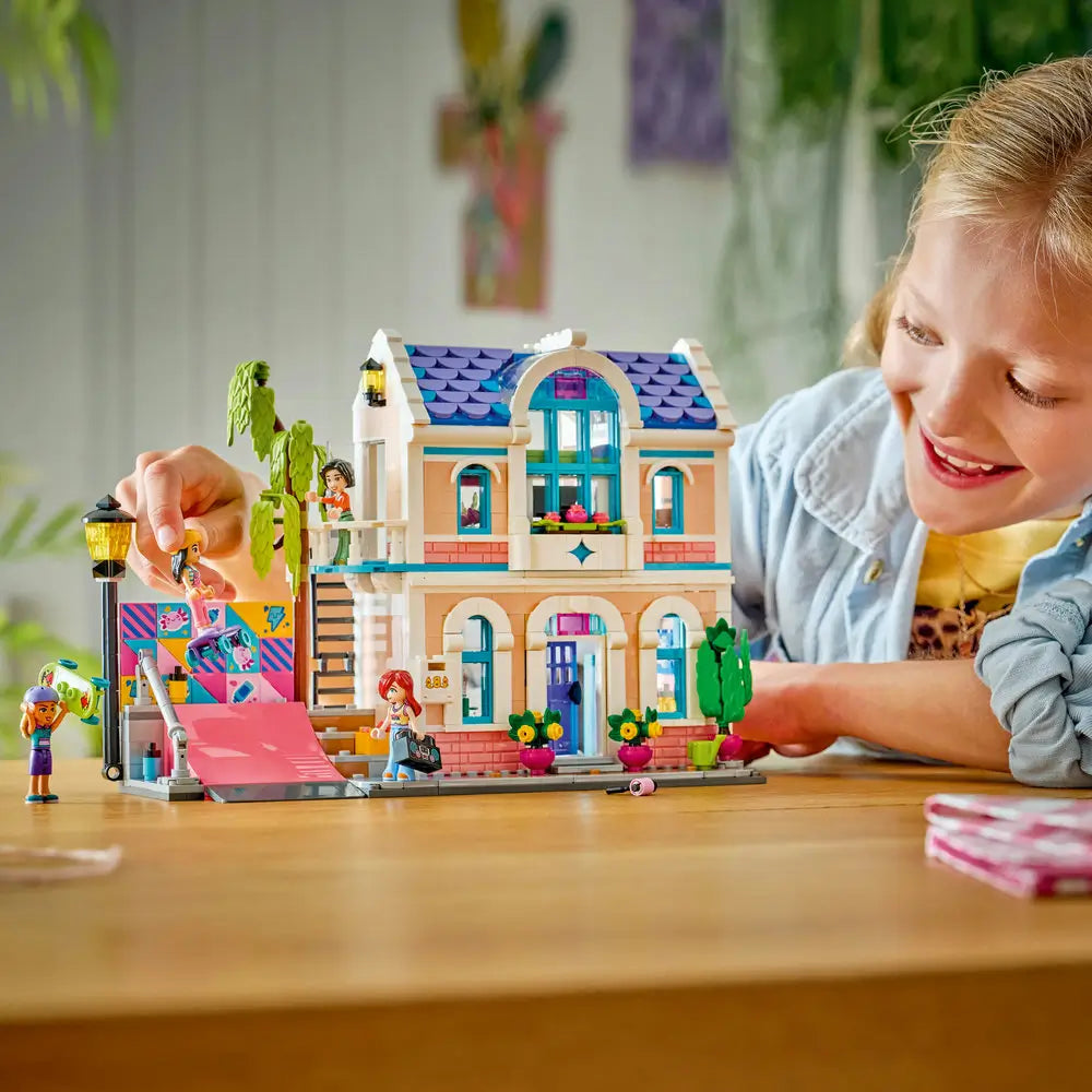 LEGO Friends playset lifestyle scene with a smiling child interacting with a completed pastel brick family house, moving minifigures along the ramp, balcony, and sidewalk to create imaginative stories.
