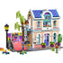 LEGO Friends house playset showing pastel peach and pink plastic bricks forming a two story family home with blue roof, balcony, ramp, plants, and minifigures arranged for imaginative neighborhood play.