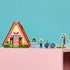 LEGO Friends Nature Glamping Cabin set in pink, yellow and brown plastic, with A-frame cabin, two mini-dolls, teal bike and flower tree displayed on a pink shelf.