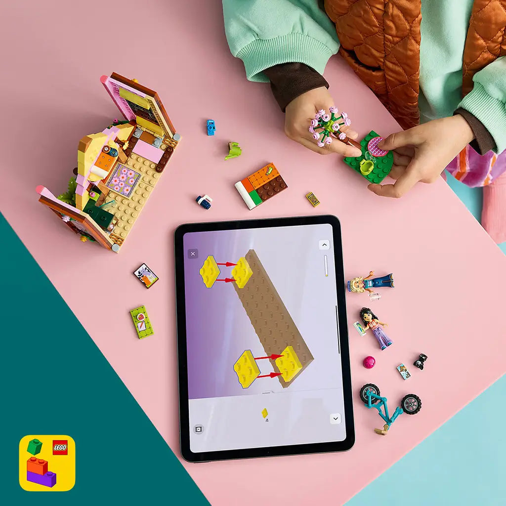 LEGO Friends Nature Glamping Cabin build in pink and brown plastic, with a child assembling flower scenery beside mini-dolls, bike parts and tablet instructions.