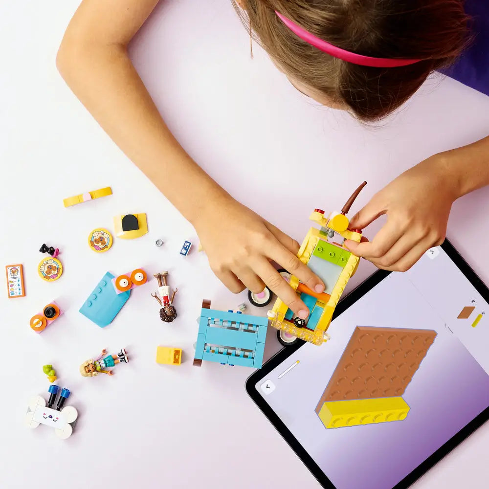 LEGO Friends lifestyle build image showing a child connecting yellow and teal plastic bricks to form the pet accessories van, while pets, wheels, roof panels, and decorative elements are arranged nearby.