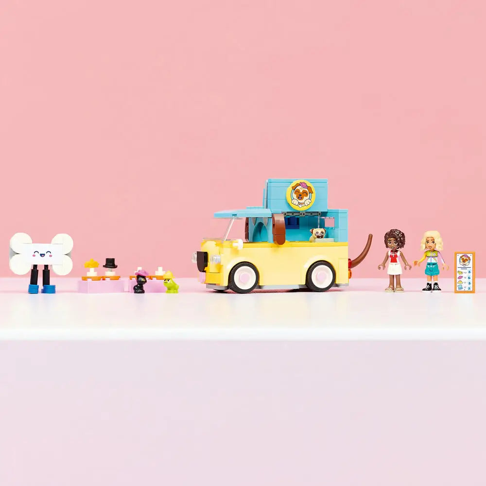 LEGO Friends pet van display showing a finished yellow and teal plastic vehicle with dog logo, rolling wheels, service counter, accessories, minidolls, pet figures, and clean studio background.