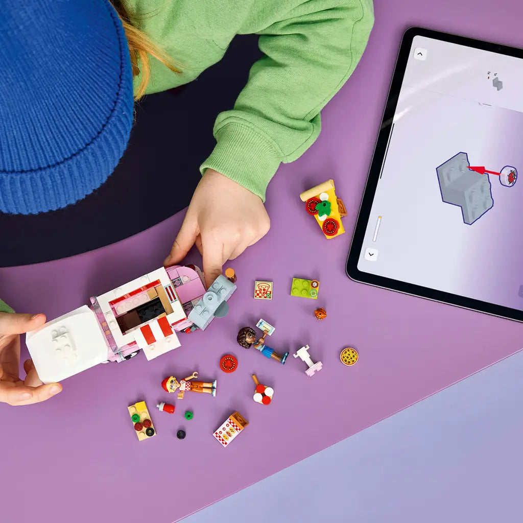 LEGO Friends Pizza Truck set in pink, red, white and gray plastic, under construction with loose pieces and mini-dolls beside digital building instructions.