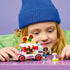 LEGO Friends Pizza Truck set in pink, red, white and gray plastic, with two mini-dolls and pizza accessories as a child plays at a purple table during imaginative play.
