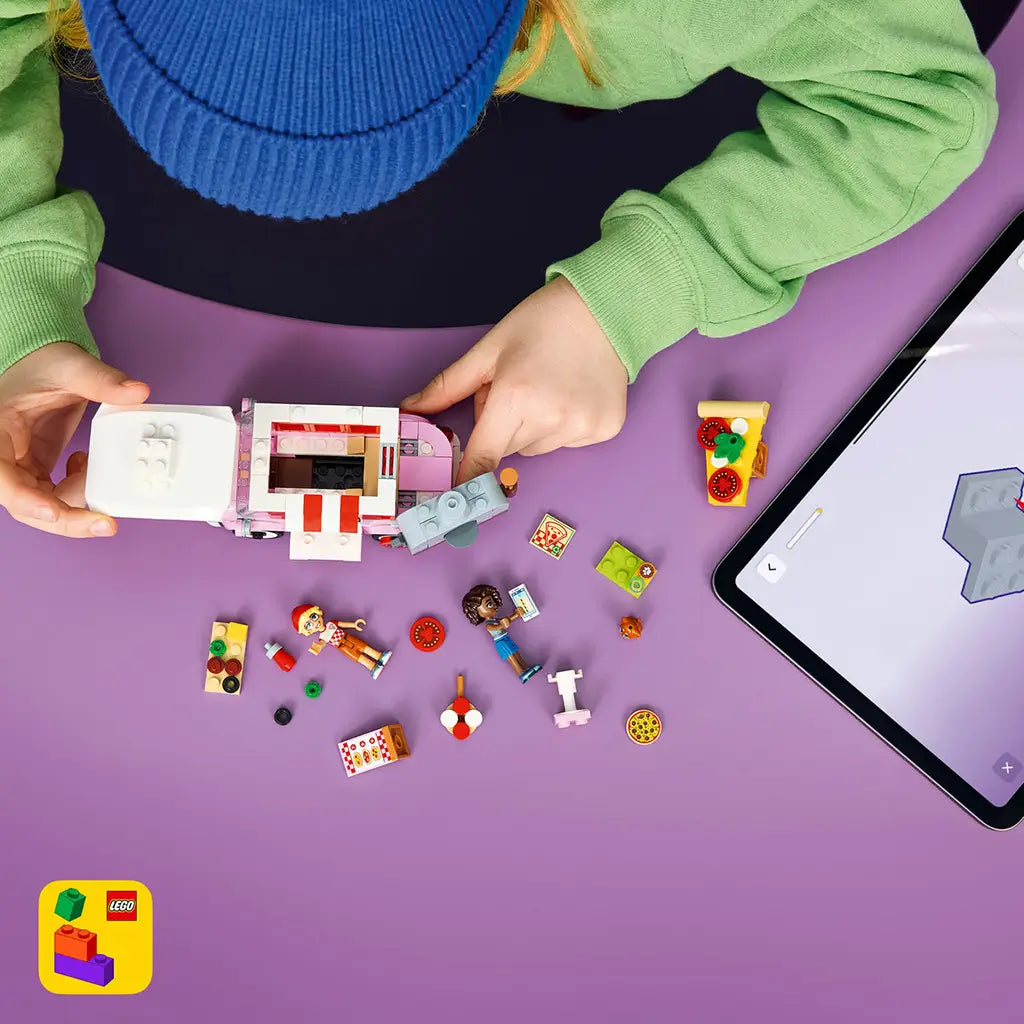 LEGO Friends Pizza Truck set in pink, red, white and gray plastic, shown partly assembled with mini-dolls and loose pieces beside digital building instructions.