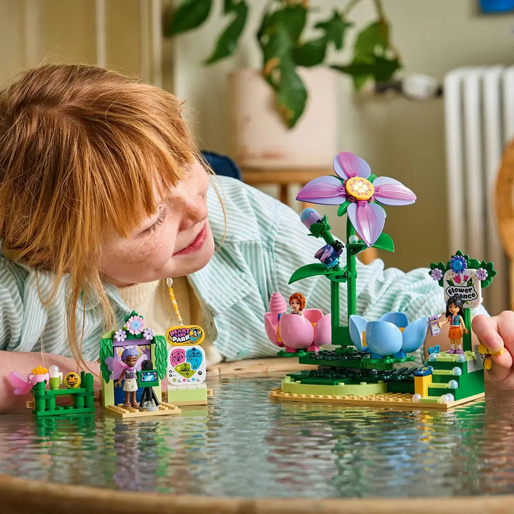 LEGO Friends Spinning Flower & Fairy Teacup Ride features pink, blue and green plastic flower seats as a child plays with the colorful amusement park set on a table.