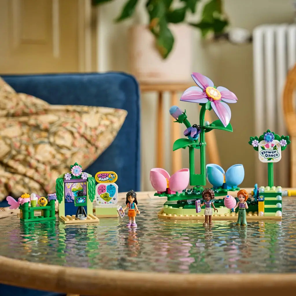LEGO Friends Spinning Flower & Fairy Teacup Ride display features pink and blue flower seats, a tall purple flower, three mini-dolls and park signs on a reflective table.