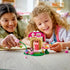 LEGO Gabby's Dollhouse garden house in pink, tan and green plastic bricks is used for play by a child and adult, with fairy figure, cat character and flower accessories.