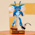 LEGO Cornish Pixie model posed mid-air with translucent wings spread, blue body and antennae visible, displayed on a brown book-themed base with wand and inkwell accessories in a lifestyle setting.
