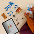 Builder assembling LEGO Cornish Pixie set with blue body parts, translucent wings, book base, and accessories laid out on a table, following digital building instructions on a tablet.