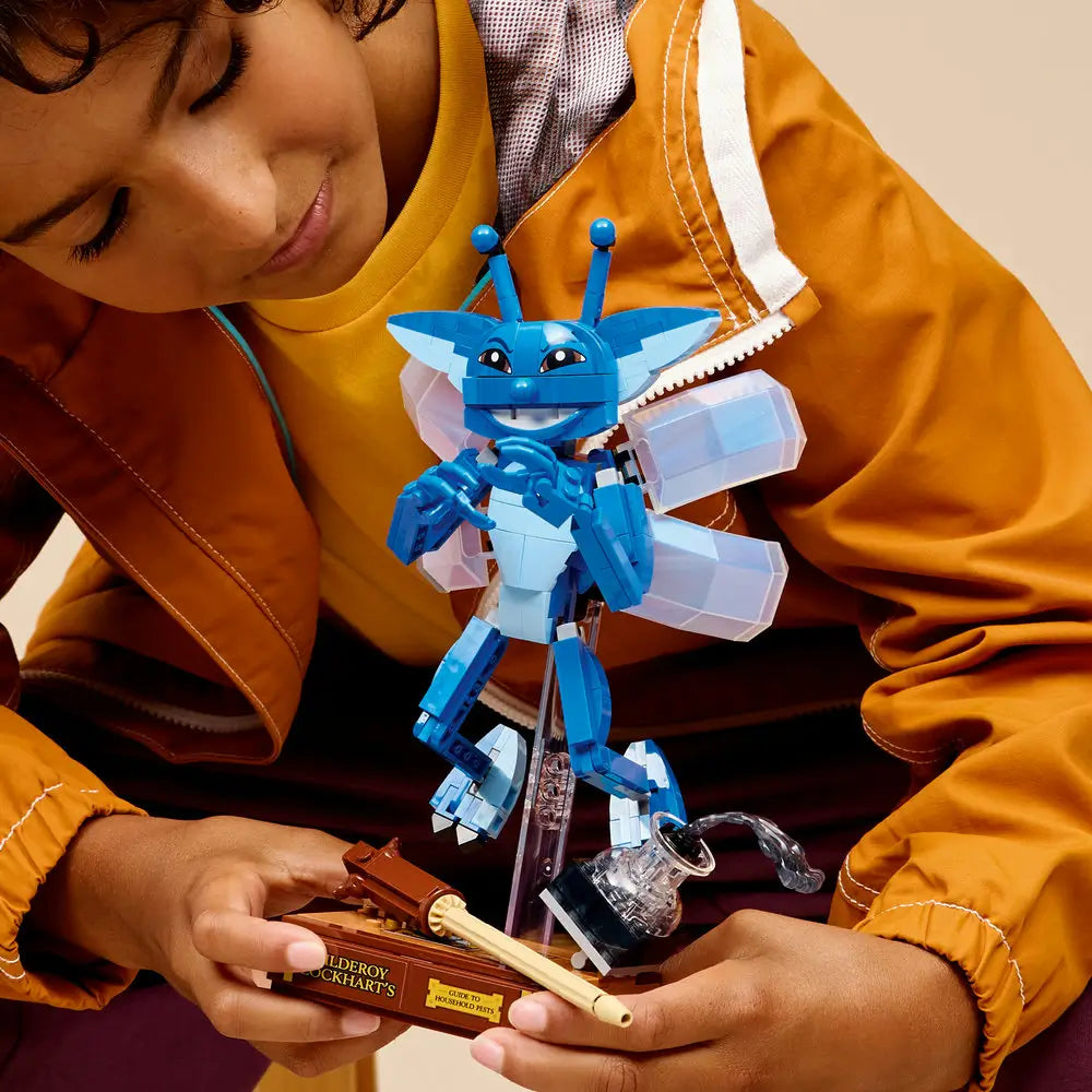Child holding and examining the completed LEGO Cornish Pixie model, showing its poseable limbs, wings, and book-themed base with wand accessory.