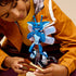 Child holding and examining the completed LEGO Cornish Pixie model, showing its poseable limbs, wings, and book-themed base with wand accessory.