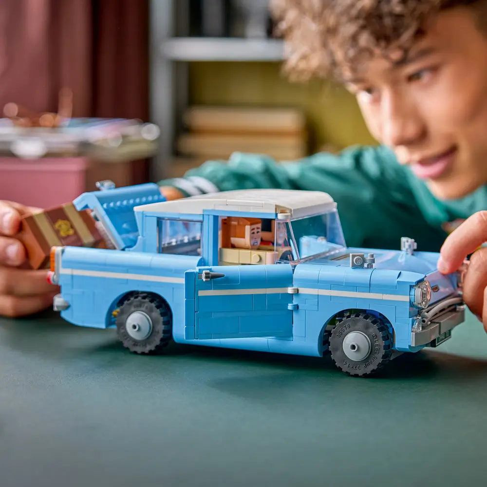 Child assembling LEGO Harry Potter Enchanted Flying Ford Anglia made of light blue plastic with opening doors and removable roof, holding pieces at hand scale to show interactive building and creative play indoors.