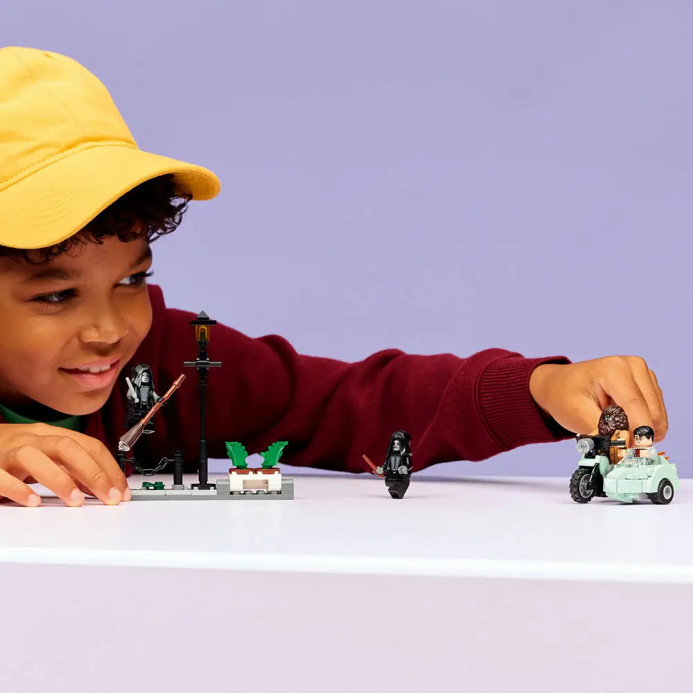 LEGO Harry Potter lifestyle builder scene shows a child’s hands assembling gray and green plastic street elements, plants, and lamp post pieces while following step-by-step digital instructions displayed on a tablet nearby.