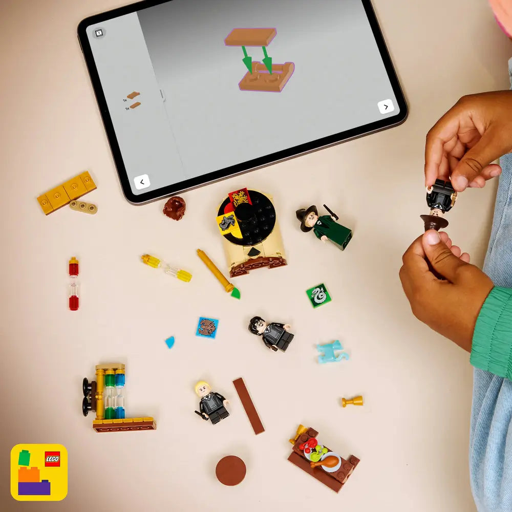 LEGO Harry Potter building experience shows multicolor plastic bricks, minifigures, and accessories scattered on a light tabletop as hands assemble pieces, guided by a tablet displaying step-by-step digital instructions above.