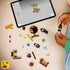 LEGO Harry Potter building experience shows multicolor plastic bricks, minifigures, and accessories scattered on a light tabletop as hands assemble pieces, guided by a tablet displaying step-by-step digital instructions above.