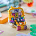 LEGO Altar of the Dead opens into a colorful brick altar with yellow flowers, framed animal art, bottles, candles, food offerings, and a skull on a tabletop.