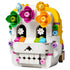LEGO Altar of the Dead skull in white plastic bricks has a rounded form with black eye sockets, colorful flower decorations, yellow trim, and a toothy grin on white.