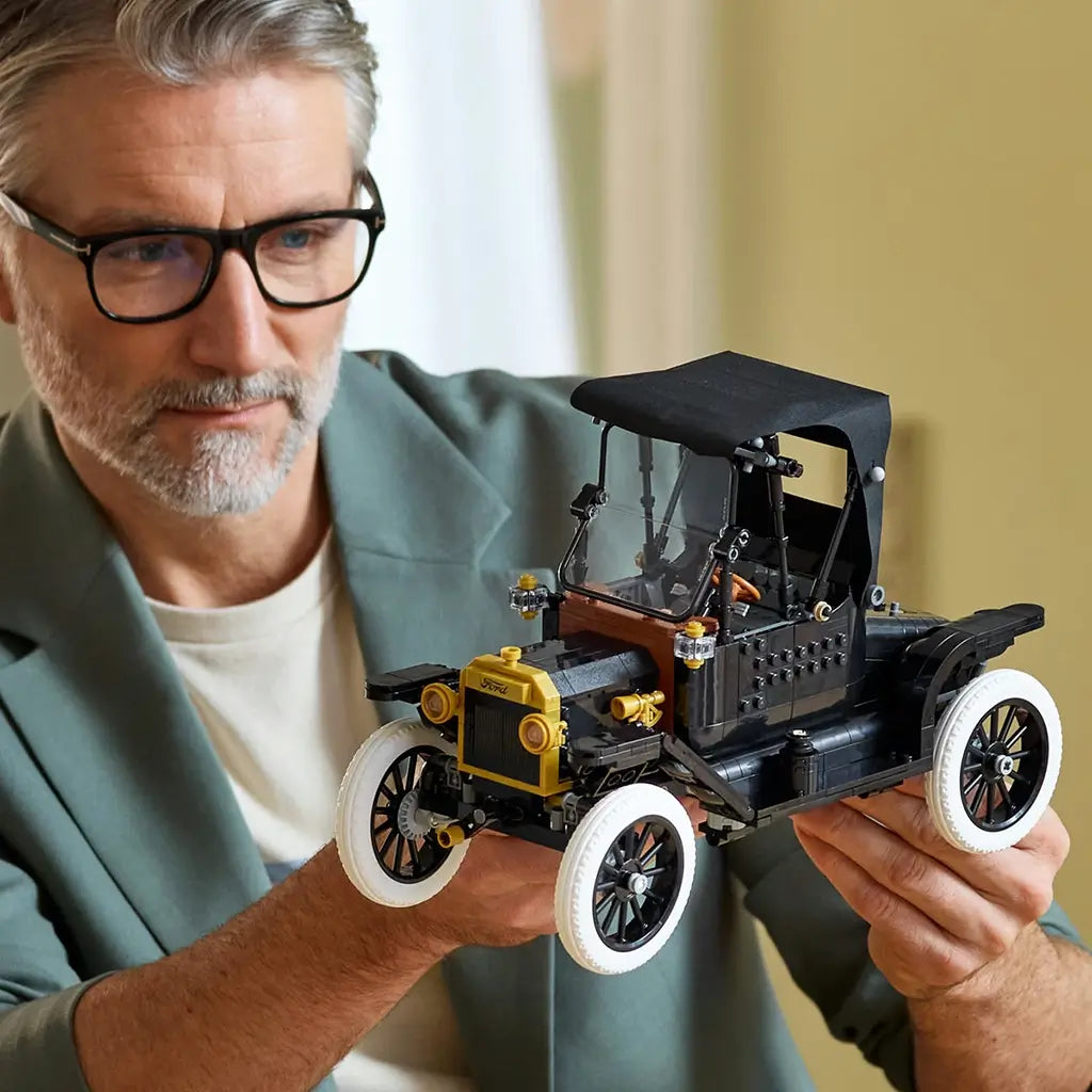 LEGO Ford Model T model shows black plastic body with gold trim and white tires, held by an adult in a home setting, highlighting detailed vintage car design and hands-on building experience.
