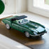 LEGO Icons Jaguar E-Type display features a dark green brick-built roadster with black soft top, clear windshield and silver wire wheels resting on a wood surface by a window.